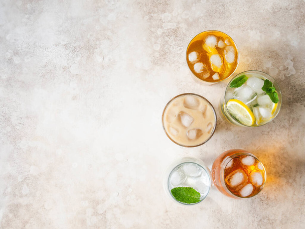 Flat lay of various refreshing drinks in glasses with ice. Apple juice, homemade lemonade, iced coffee, iced tea and sparkling water on beige background. Top view - Zdjęcie, obraz