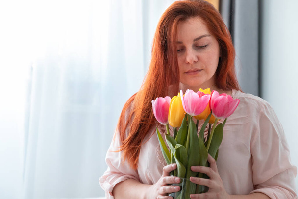 Bella ragazza dai capelli lunghi che tiene un mazzo di fiori di tulipani freschi nella stanza. Sorriso sul viso, San Valentino, concetto di compleanno
 - Foto, immagini