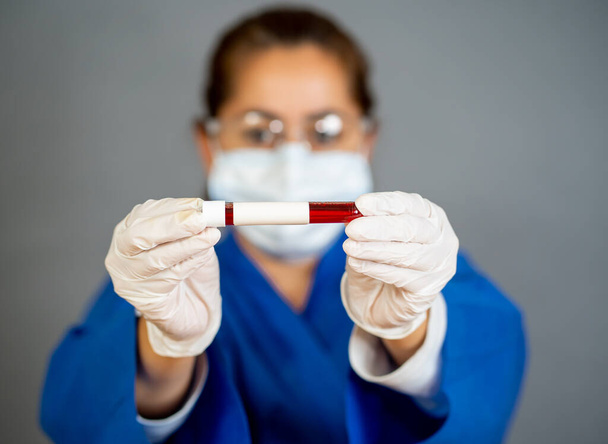 COVID-19. Doctor or lab technician scientist in PPE Personal Protective Equipment holding blood sample tube of infected patient at hospital. Coronavirus blood test for antibodies and vaccine research. - 写真・画像