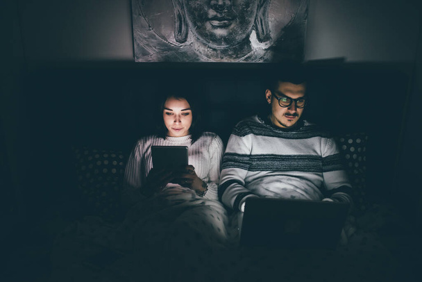 Yatakta yatan çiftler, teknolojik cihazlar kullanarak yatıyorlar. Sahtekarlık, görmezden gelme, bağımlılık yapan konsept. - Fotoğraf, Görsel