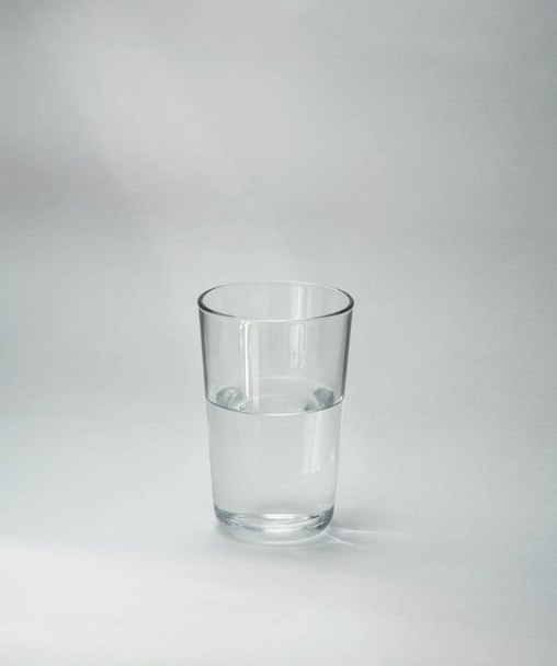 Una taza de vidrio medio llena de agua se encuentra sobre un fondo claro. Primer plano. Copiar espacio
 - Foto, Imagen