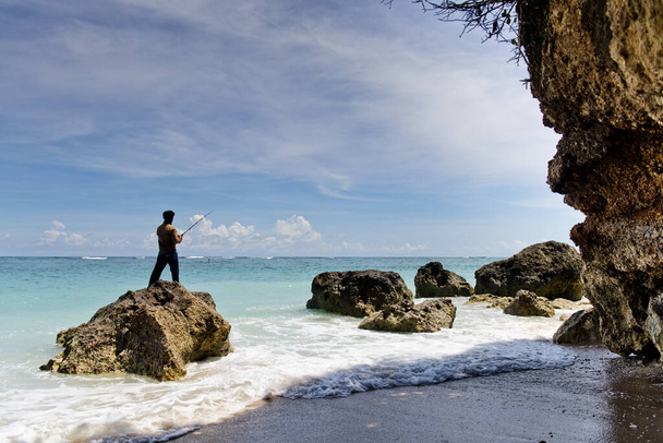 Молодой человек стоит на пляже и рыбачит. Пляж Пандава, Бали, Индонезия
. - Фото, изображение