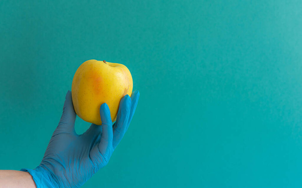 Luvas médicas de látex azul na mão de uma mulher, palma estendida. Mãos de luva de mulher segurando uma maçã, mãos de luva, mãos de mulher, luvas médicas azuis, maçã amarela
 - Foto, Imagem