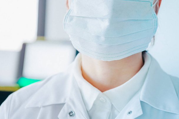 młoda kobieta w medycznej masce ochronnej twarzy w pomieszczeniach na tle laboratoryjnym - Zdjęcie, obraz