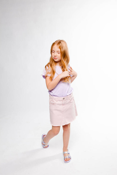 rudowłosy długowłosy dziewczyna w codziennych ubraniach (spódnica, T-shirt) warkocze jej włosy - Zdjęcie, obraz