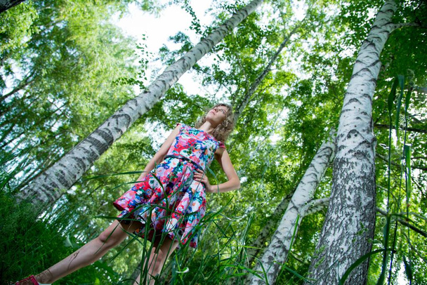 Genç ve güzel bir kadın huş ağaçlarının yanında poz veriyor. Çiçekli elbiseler giyiyor. - Fotoğraf, Görsel