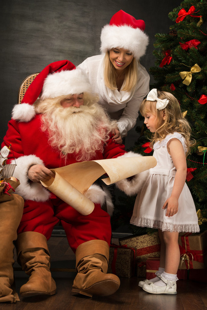 Santa Claus sitting at home with cute little girl and her mother - Фото, зображення