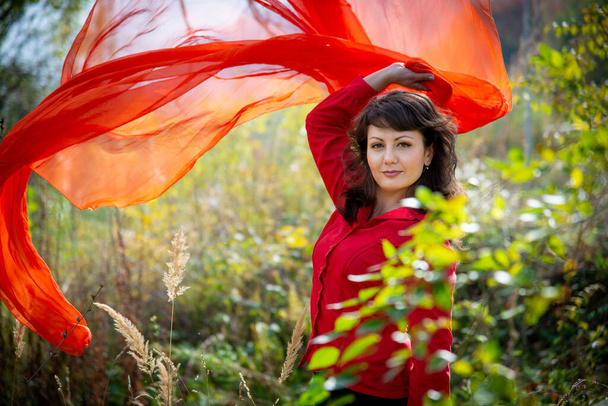  young beautiful woman posing outdoors with bright red scarf  - Photo, Image