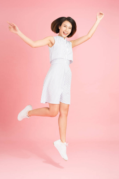 Ελευθερία στην κίνηση. Έκπληκτη, όμορφη, χαρούμενη νεαρή γυναίκα πηδάει και κάνει χειρονομίες σε ροζ φόντο στούντιο. - Φωτογραφία, εικόνα