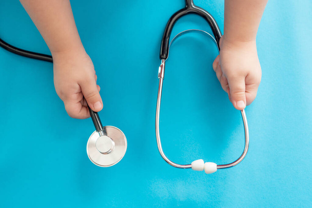 Children's hands hold a medical stethoscope on a blue background. - Photo, image