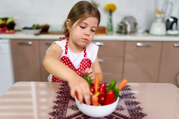 Little girl arranging various vegetables into a bowl - Fotografie, Obrázek