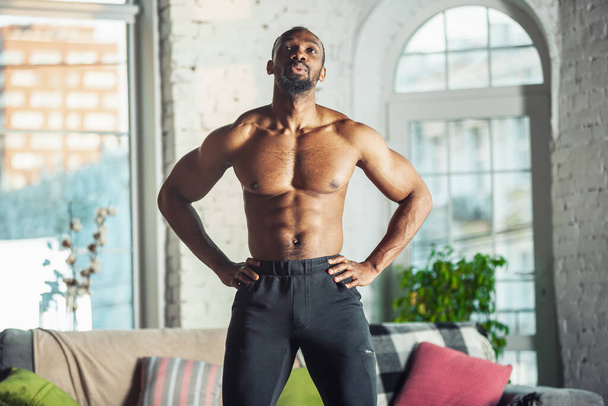 Young african-american man teaching at home online courses of fitness, aerobic, sporty lifestyle while being quarantine - Valokuva, kuva