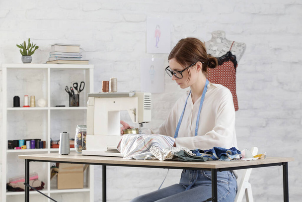 Vrouw naaien op naaimachine in kleine studio, mode atelier, slow fashion, tailor ambachtelijke, handgemaakte kleding - Foto, afbeelding