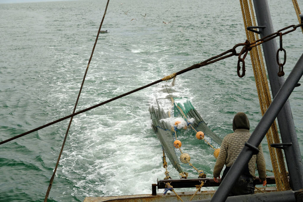 Fischer bei der Arbeit. Matrosen ziehen das Schleppnetz mit dem Fang auf das Deck des Schiffes. Fisch im Netz gefangen. Angeln. Schwarzes Meer. Überwiegend bewölkt. - Foto, Bild