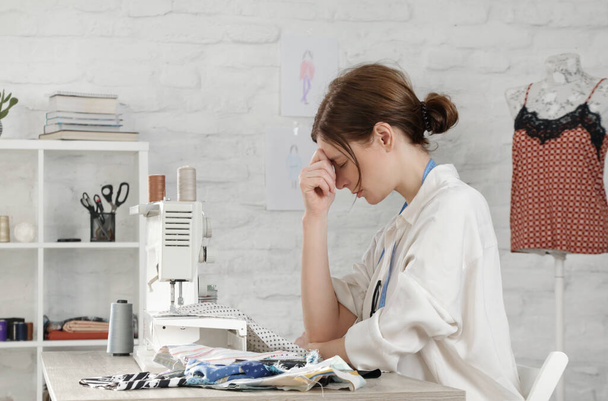 Sleepy, frustrated, exhausted seamstress with headache on her work desk. Small business or self-employed problems. Deadline or overwork concept, bored or getting tired at work in creative industry. - 写真・画像
