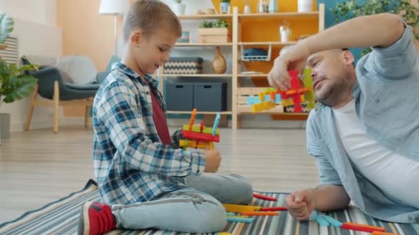 Joyful family dad and son having fun with wooden toys relaxing laughing at home - Materiał filmowy, wideo