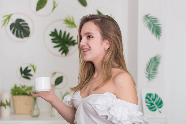 Mujer joven bebiendo té sentado en el hermoso interior con flores verdes en el fondo. Lindo retrato de joven diseñador y florista, estudiante
. - Foto, Imagen