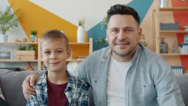 Portrait of two people young adult father and cute little son smiling on sofa at home - Materiał filmowy, wideo