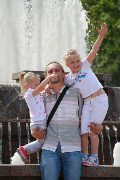 father holds two daughters in his arms on the background of the fountain - Photo, Image