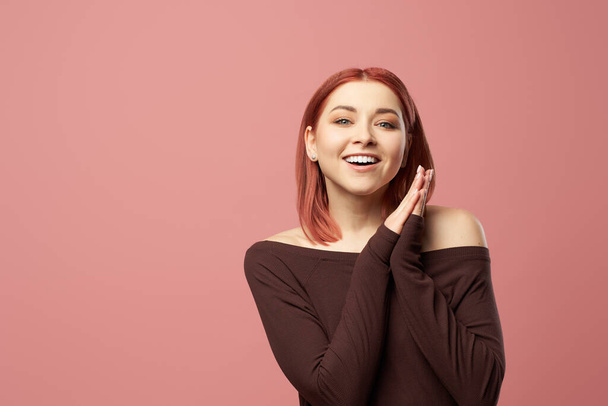 Smiling ginger girl in burgundy sweater isolated on empty pink background - Фото, изображение