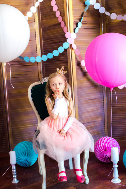 Little cute girl with blond hair in a pink dress and a princess crown with large bright balloons and garlands. Children's holiday. Children's decor. Balloons - Фото, изображение