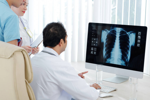Pulmonologue et ses assistants examinant la radiographie pulmonaire du patient à l'écran de l'ordinateur
 - Photo, image