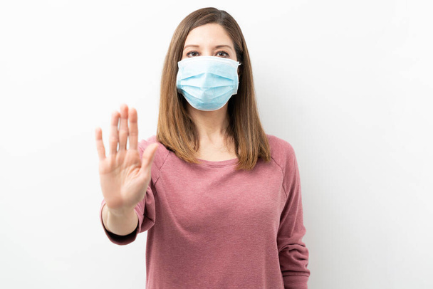 Žena brunetka na sobě chirurgické masky a dělat stop gesto s rukou ve studiu - Fotografie, Obrázek