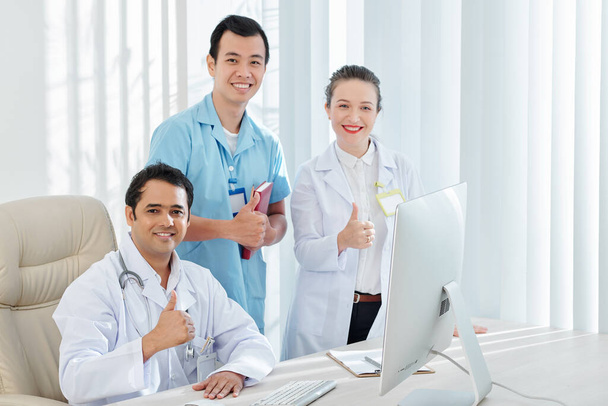 Glimlachende huisarts, chirurg en cardioloog met duimen omhoog - Foto, afbeelding