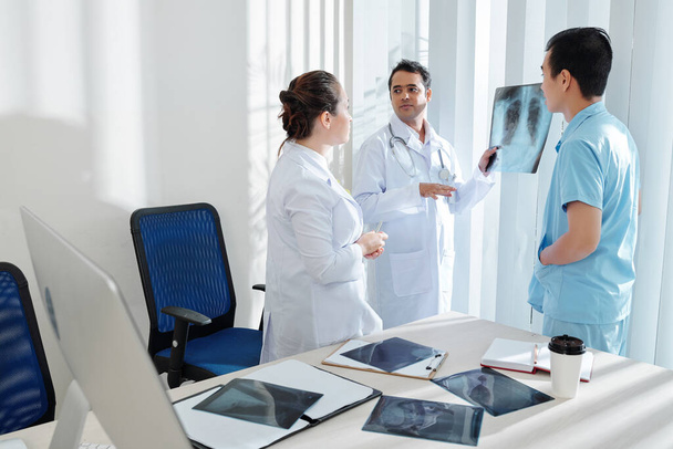 Doctor mostrando radiografía de tórax del paciente con virus peligroso a sus compañeros de trabajo y discutiendo el tratamiento
 - Foto, imagen