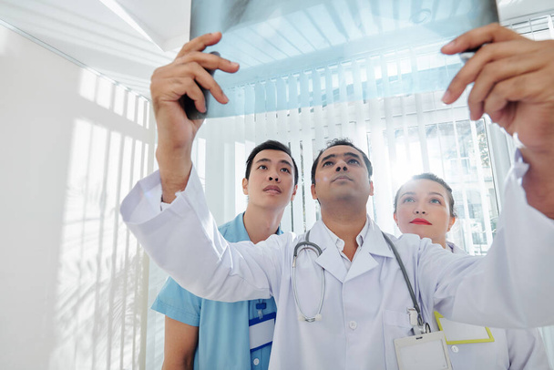Wieloetniczna poważna grupa lekarzy badających prześwietlenie pacjenta - Zdjęcie, obraz
