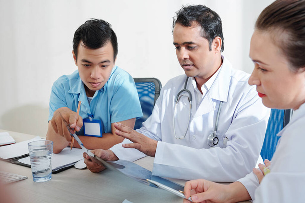Grupa ciężkich pracowników medycznych omawiających prześwietlenie płuc pacjenta z objawami koronawirusa - Zdjęcie, obraz