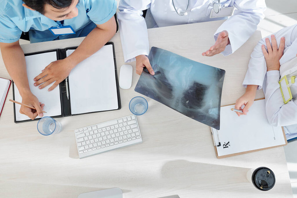 Médico geral e seus estagiários discutindo pulmões raio-X do paciente, escrevendo sintomas e prescrição
 - Foto, Imagem