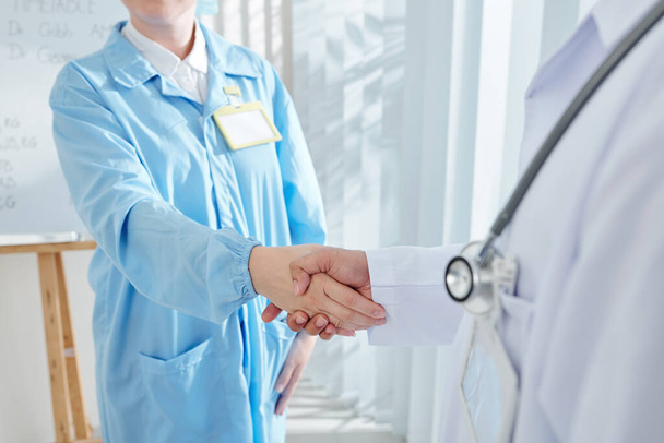 Huisarts met stethoscoop op zijn borst schudden hand van verpleegkundige - Foto, afbeelding