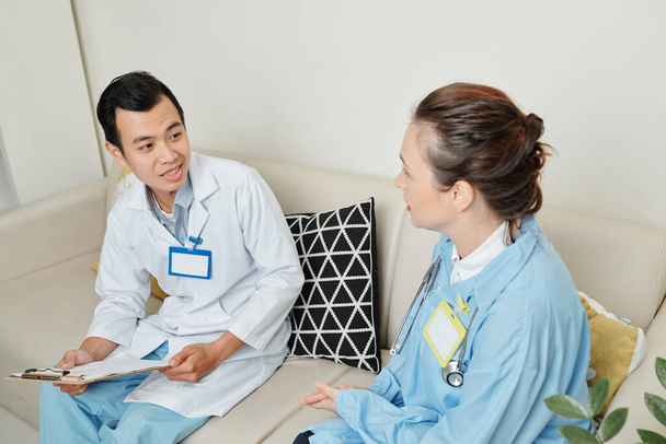 Nuori aasialainen harjoittelija kysyy lääkäriltä neuvoja diagnoosia tehtäessä
 - Valokuva, kuva