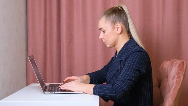 Seriöse Sekretärin tippt auf einem Laptop, der an einem Tisch an seinem Arbeitsplatz sitzt. - Foto, Bild