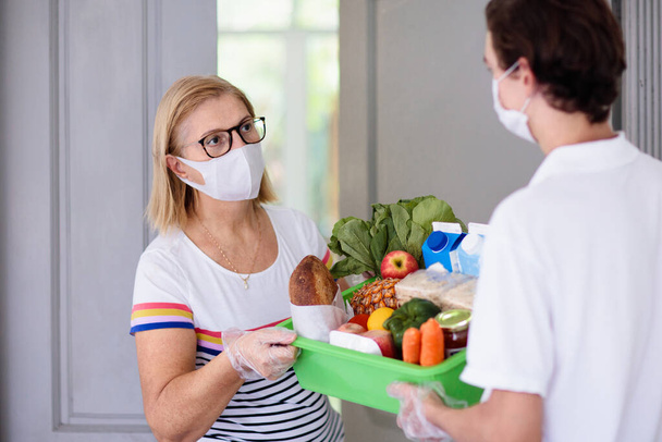 Food delivery during corona virus outbreak. Courier wearing face mask delivering grocery order in coronavirus epidemic. Safe shopping in pandemic. Takeout meal. People stockpile food. - Photo, Image