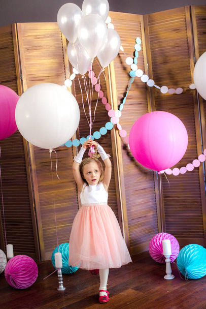 Little cute girl with blond hair in a pink dress and a princess crown with large bright balloons and garlands. Children's holiday. Children's decor. Balloons - Фото, зображення