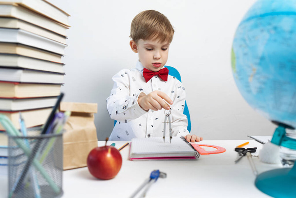 Back to school: A boy sits at a desk and draws in a notebook using a compass. - Fotoğraf, Görsel