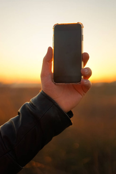 Ruka drží telefon na pozadí slunce. Detailní záběr - Fotografie, Obrázek