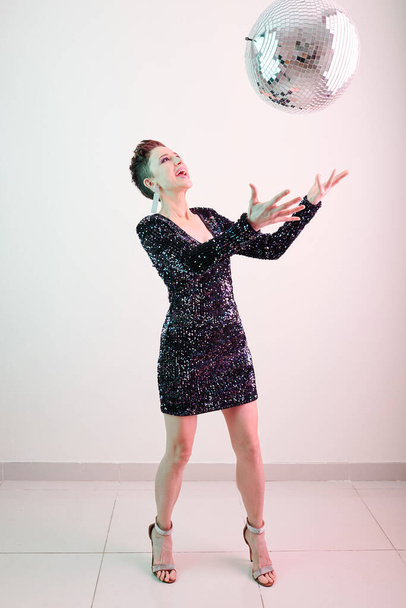Studiofoto einer Frau in kurzem, glänzendem Kleid, die Partyball wirft - Foto, Bild