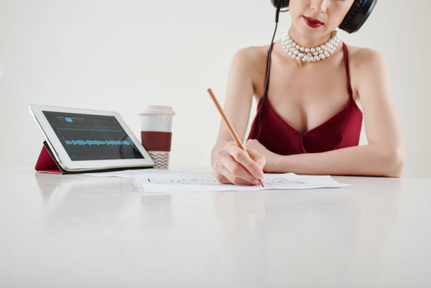 Immagine ritagliata di musicista donna di talento seduta alla scrivania e che scrive musica e nuove canzoni - Foto, immagini