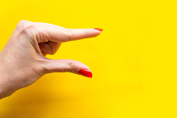 Closeup άποψη του γυναικείου χέρι που σχηματίζουν χειρονομία Λίγο. Απομονωμένα σε φωτεινό κίτρινο φόντο.  - Φωτογραφία, εικόνα
