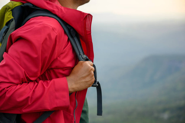 Wanderer, die in einer roten Regenjacke mit einem Rucksack am Rande einer Klippe stehen Sehen Sie die Schönheit der Berge bei Sonnenuntergang und zeigen Sie Erfolg, Freiheit und Abenteuer. - Foto, Bild
