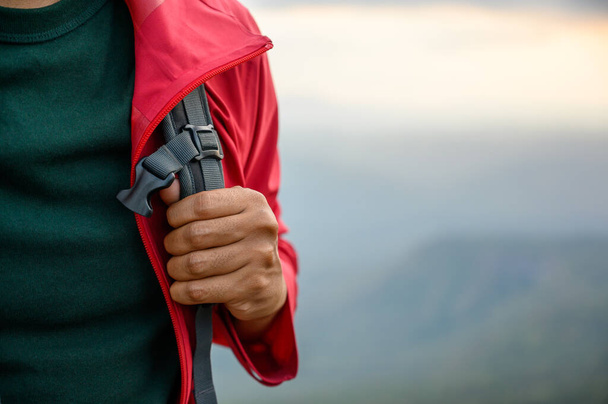 Wanderer, die in einer roten Regenjacke mit einem Rucksack am Rande einer Klippe stehen Sehen Sie die Schönheit der Berge bei Sonnenuntergang und zeigen Sie Erfolg, Freiheit und Abenteuer. - Foto, Bild
