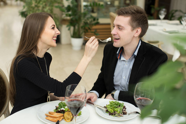 Beautiful young couple feeding each other and smiling while spending time at the restaurant. - Photo, Image