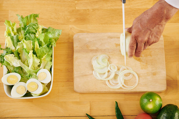 Kıdemli adam salata pişirirken tahtada taze soğan kesiyor, yukarıdan görüyor. - Fotoğraf, Görsel
