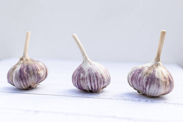 Three garlics on a white wooden table. Folk remedy for increasing immunity. Useful fruit from the garden. - Photo, Image