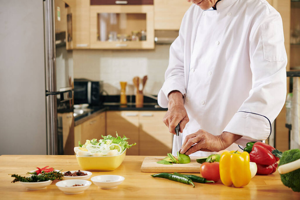 Uomo in giacca bianca chef ingredienti di taglio per una sana deliziosa insalata nella sua cucina - Foto, immagini