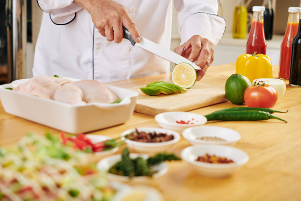 Man cutting lime on wooden board when preparing marinade for chicken - Photo, Image