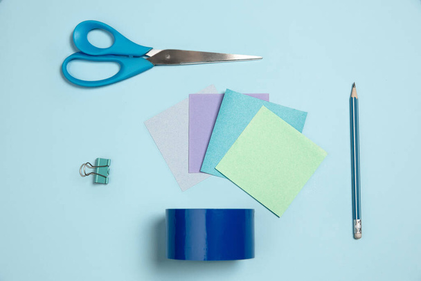 Papeles engomados, tijeras, bolígrafo. Composición elegante monocromática en color azul. Vista superior, plano
. - Foto, Imagen